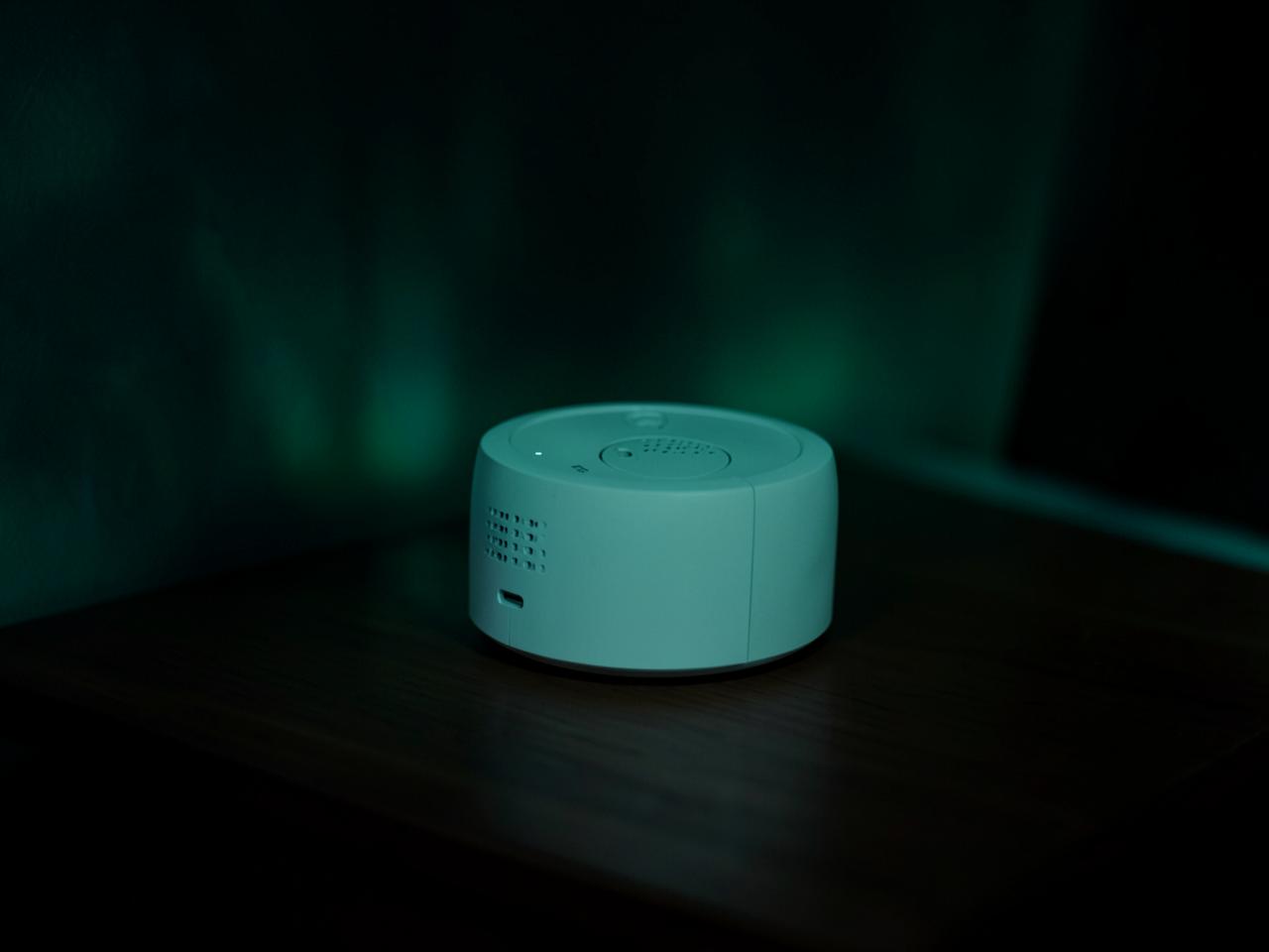 Detalle del proyector blanco sobre una mesita de noche con luz verde de aurora